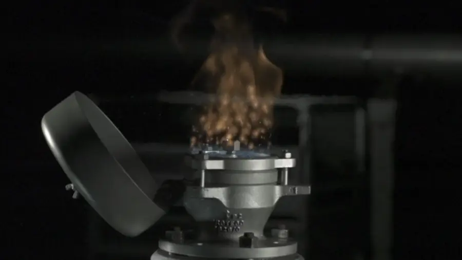 Close-up of an industrial flame arrester or valve emitting a controlled flame plume from its top during a dark, controlled ignition test.
