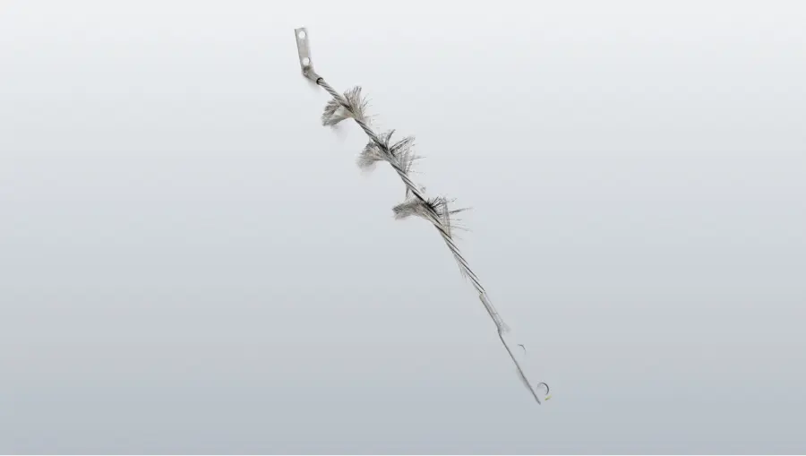 A twisted metal wire brush with several tufts of gray bristles and flat mounting tabs at both ends on a white background.
