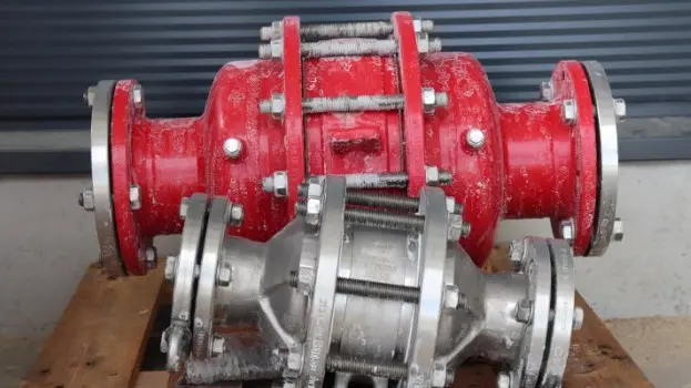 Two industrial inline safety devices or flame arresters, one red and one silver, resting on a wooden pallet with visible frost residue in an outdoor setting.