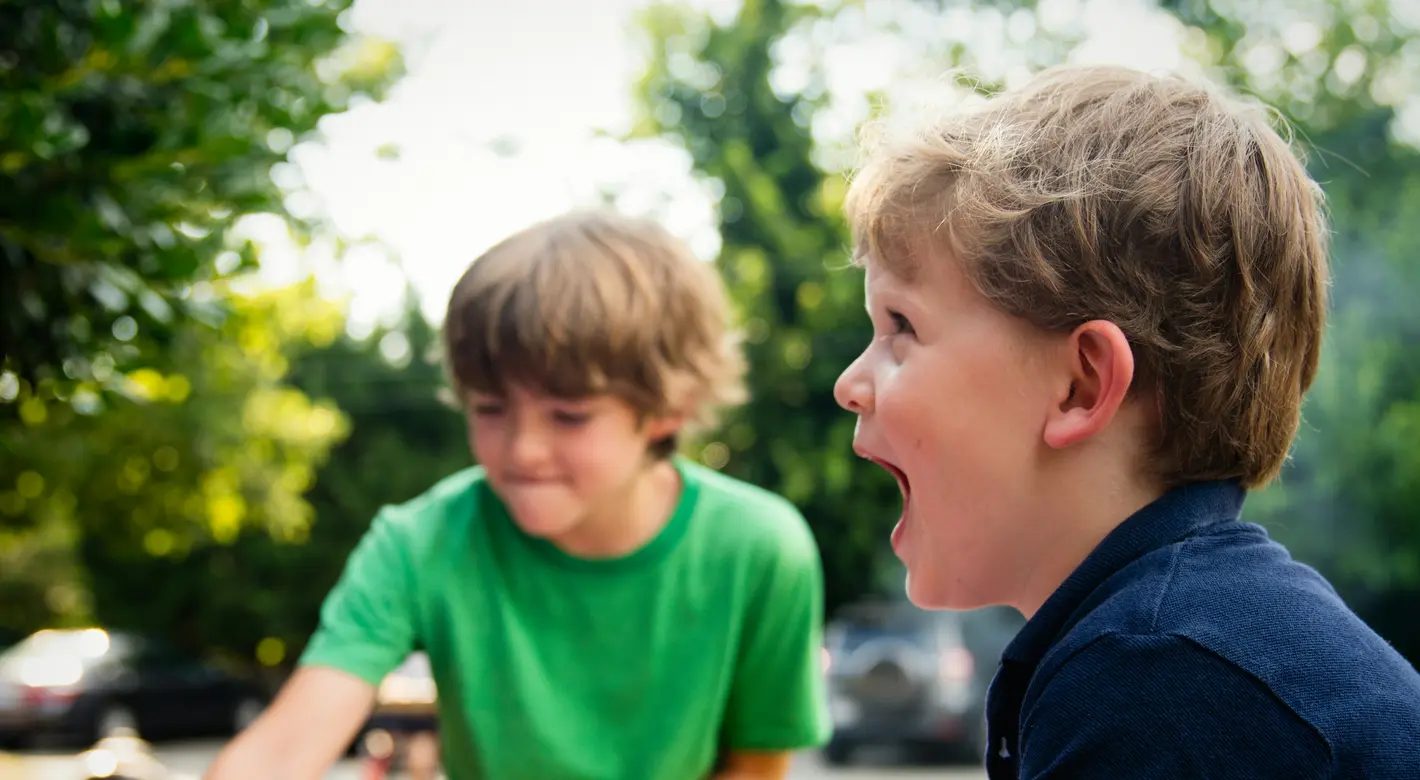 Two boys play at a small pink inflatable pool outdoors, with one boy laughing in the foreground.