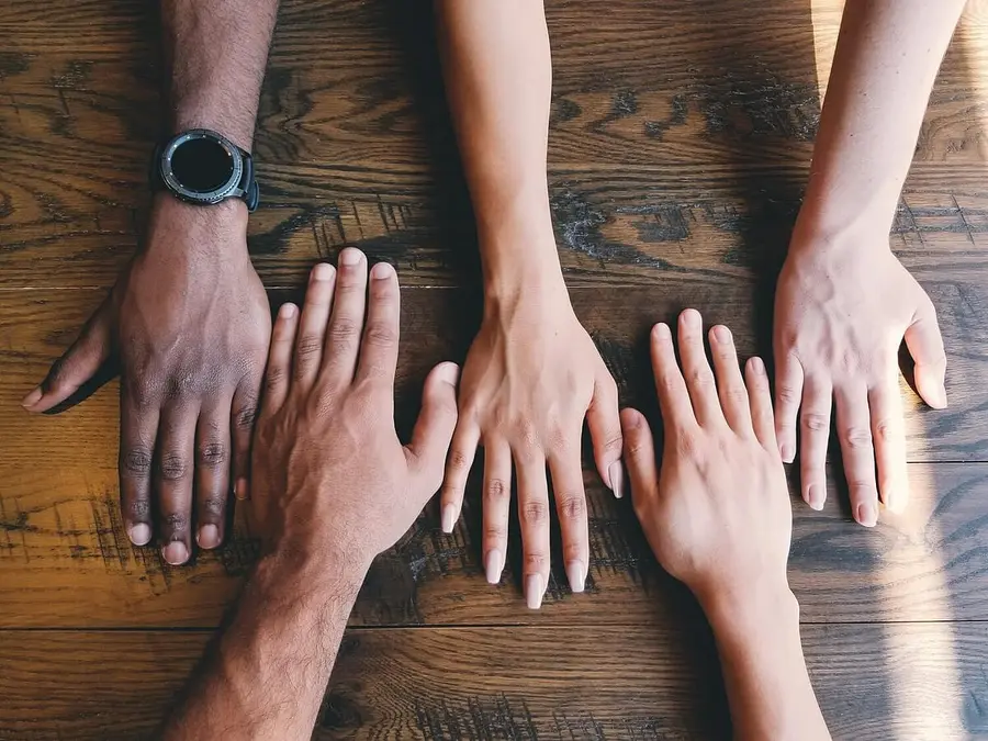 Four hands of different individuals laid out on a wooden table, symbolizing unity and collaboration.