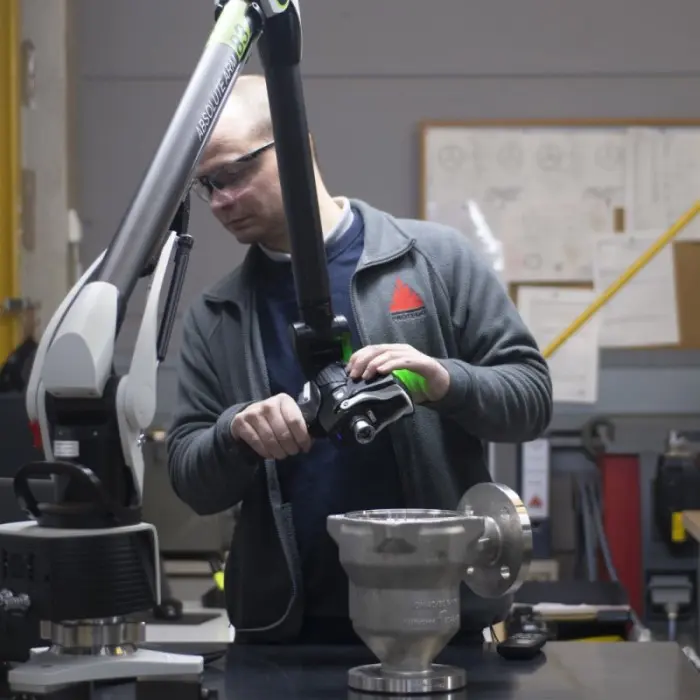 A technician uses a 3D measuring arm to inspect a metal industrial component in a workshop.