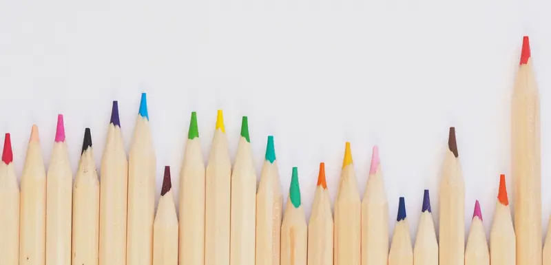 Une rangée de crayons de couleur bien taillés longe le bord inférieur d'un fond blanc, laissant un espace vide au-dessus.