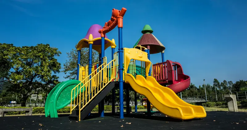 Une aire de jeux colorée, équipée de toboggans et de structures d'escalade, se dresse sous un ciel d'un bleu limpide.