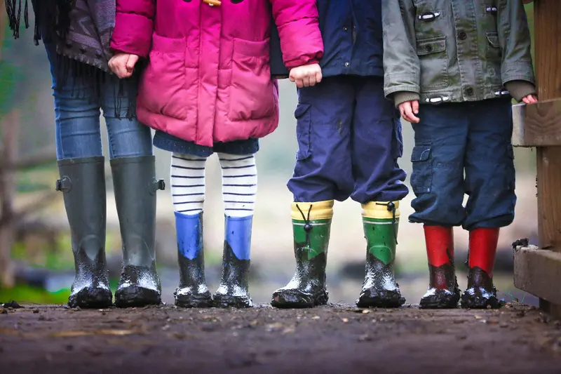 Close-up of an adult and three children standing in muddy wellington boots, showing only their legs and coats.